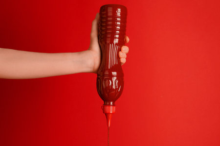 Woman squeezing ketchup out of bottle on red background, closeupの写真素材