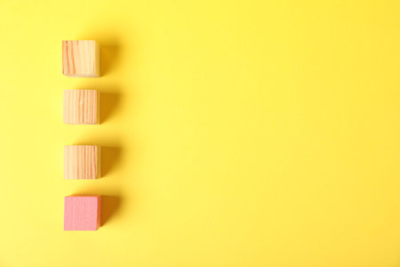 Wooden cubes and pink one on yellow background, flat lay. Space for text