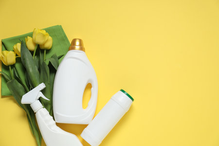 Spring cleaning. Bottles with detergents, rag and tulips on yellow background, flat lay. Space for textの写真素材