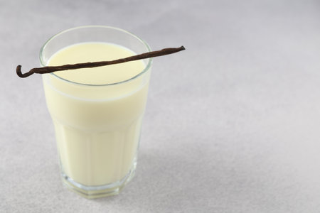 Delicious vanilla milk in glass and pod on grey table, closeup. Space for textの写真素材