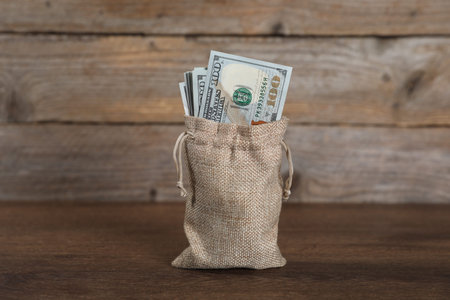 Dollar banknotes in burlap sack on wooden table
