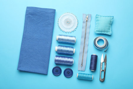 Different sewing supplies on light blue background, flat lay