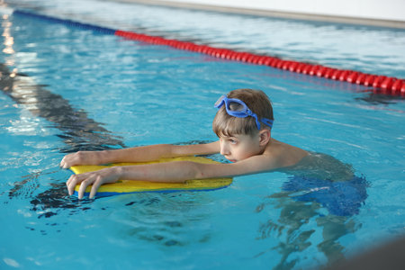 Boy with goggles and kickboard swimming pool indoorsの写真素材