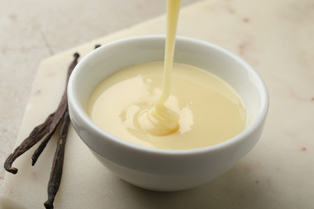 Pouring tasty vanilla condensed milk into bowl on table, closeup