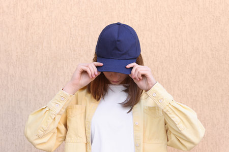 Woman in stylish baseball cap near beige wall. Mockup for design