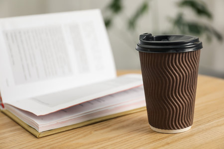 Paper cup and open book on wooden table indoors, closeup. Mockup for designの写真素材
