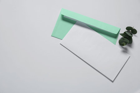 Paper envelope with letter and eucalyptus branch on white background, flat lay. Mockup for design