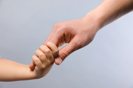 Father and child holding hands on grey background, closeupの写真素材