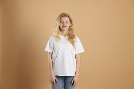 Young woman wearing blank white t-shirt on light brown background. Mockup for designの写真素材