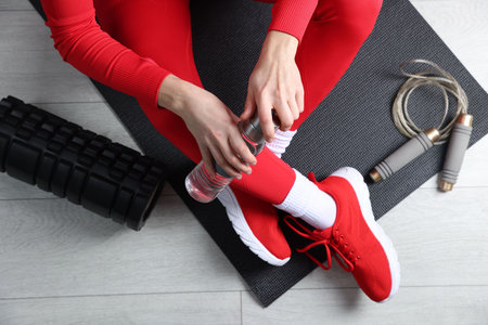 Woman with bottle of water and gym equipment on floor, top view