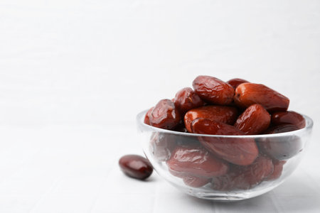 Tasty dried dates in glass bowl on white table, closeup. Space for text