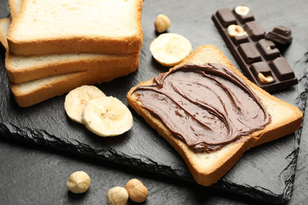 Sandwich with chocolate butter, banana and hazelnuts on black table, closeupの写真素材