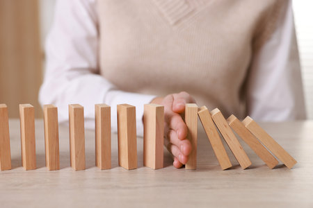 Woman stopping wooden blocks from falling at table, closeup. Domino effectの写真素材