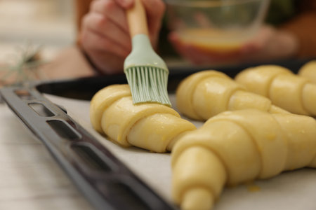 Woman brushing egg wash onto raw croissants at white table, selective focusの写真素材