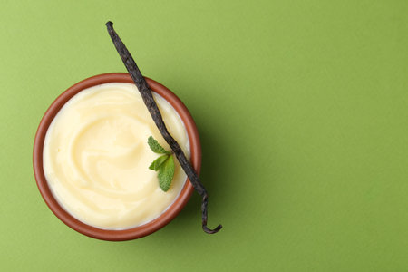 Tasty vanilla pudding, mint and pod on green background, top view. Space for textの写真素材