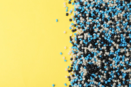Pile of colorful plastic granules on yellow background, top view. Space for textの写真素材