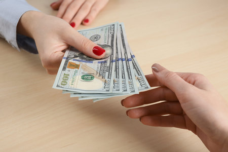 Cashier giving dollar banknotes to client at table in money exchange, closeup
