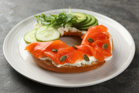 Delicious bagel with salmon, cream cheese, cucumber and pumpkin seeds on gray table, closeupの写真素材