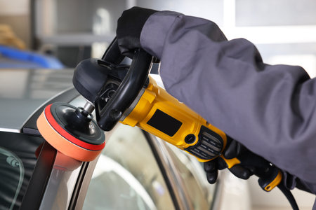 Man polishing car with orbital polisher indoors, closeup