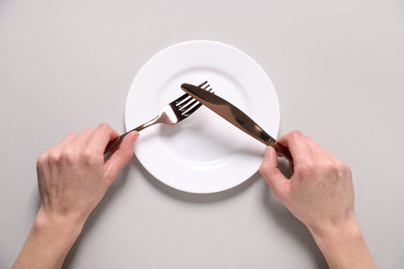 Woman with cutlery over empty plate at light table, top view