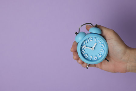 Woman with alarm clock on lilac background, closeup. Space for textの写真素材