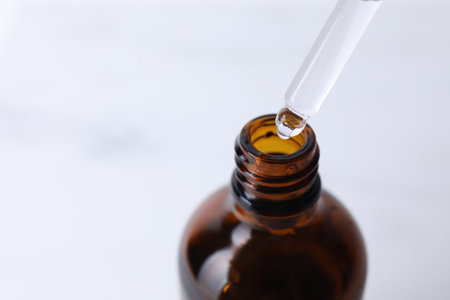 Dripping serum from pipette into bottle on light background, closeup. Space for text