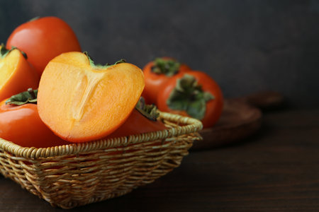 Delicious fresh juicy persimmons in wicker basket on wooden table, closeup. Space for textの写真素材