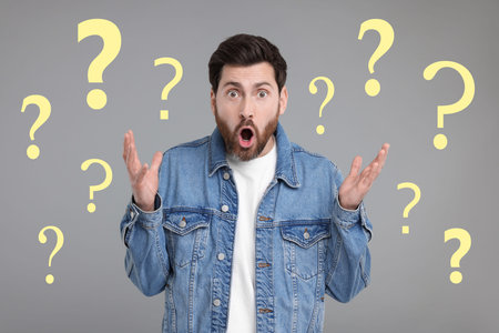Shocked man surrounded by question marks on grey background