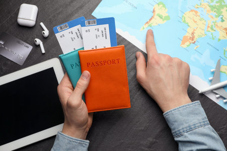 Travel agency. Man with passports and flight tickets pointing at destination on map at dark textured...