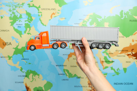 Woman with toy truck against world map, closeup. Logistics conceptの写真素材