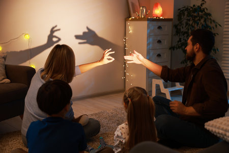 Parents making hand gestures like bunny and dog while performing shadow play to their kids at homeの写真素材