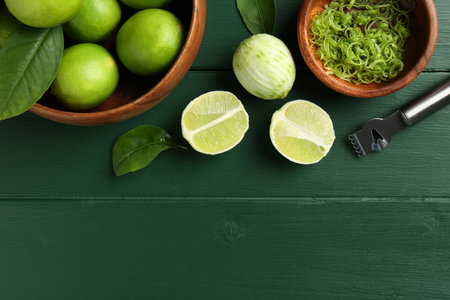 Lime zest, fresh fruits and zester tool on green wooden table, flat lay. Space for text