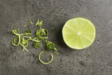 Lime zest and half of fresh fruit on grey textured table, flat layの写真素材