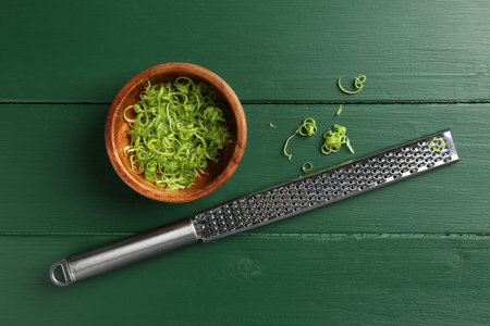 Lime zest in bowl and grater on green wooden table, flat layの写真素材