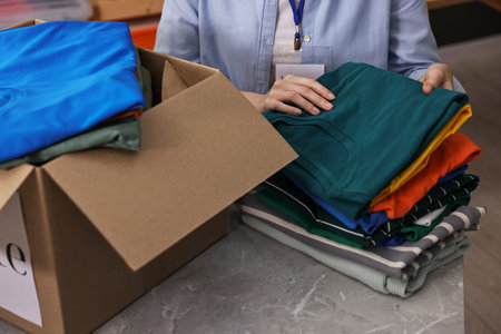 Volunteer sorting clothes for donation at table indoors, closeup