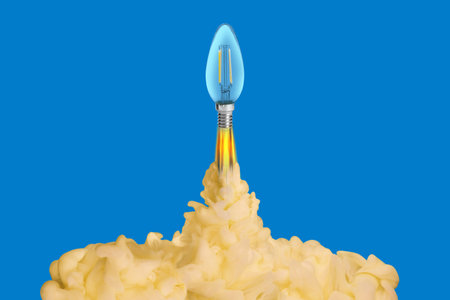 Light bulb soaring up like rocket with smoke and fire on blue background. Concepts of idea, startup,...