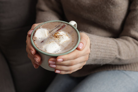 Woman holding mug of tasty hot chocolate with marshmallows and cinnamon indoors, closeupの写真素材