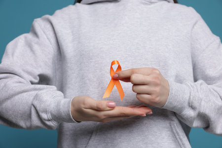 Multiple Sclerosis awareness. Young woman holding orange ribbon on light blue background, closeupの写真素材