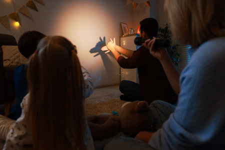Man making hand gesture while performing shadow play to his family at homeの写真素材