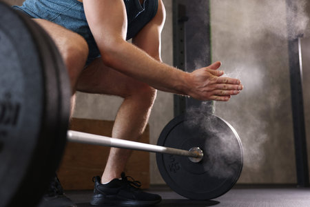 Sportsman clapping hands with talcum powder before crossfit workout with barbell in gym, closeup