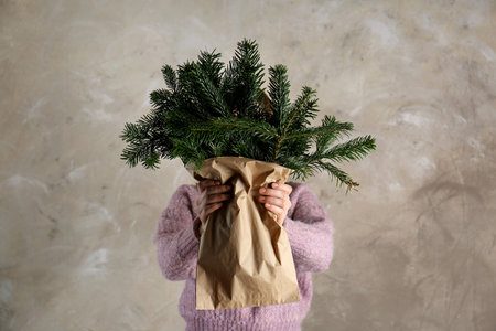 Woman holding green fir branches in paper bag near gray wall. Christmas decorの写真素材