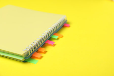 Notebook with colorful tabs on yellow background, closeup. Space for textの写真素材