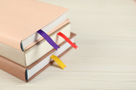 Books with ribbon bookmarks on light wooden table, closeup. Space for text