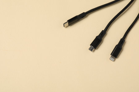 Black triple charge cable on beige background, above view. Space for text