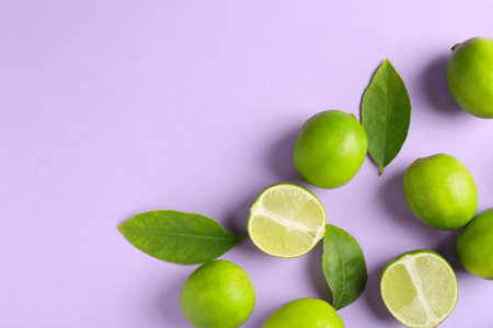 Fresh limes and leaves on violet background. Space for text