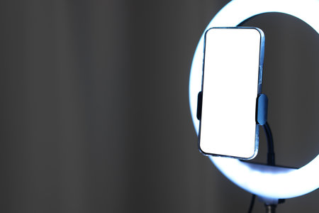 Glowing ring lamp with smartphone near grey curtain, closeup. Space for textの写真素材