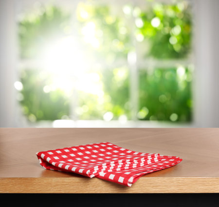 Red checkered tablecloth on wooden table in room against blurred sunlit window, closeupの写真素材
