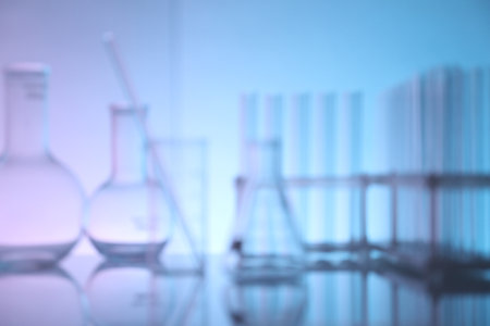 Blurred view of laboratory glassware on mirror surface against color backgroundの写真素材