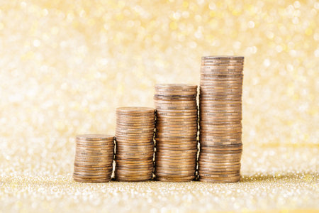 Many stacked coins on golden glitter background, closeup. Space for textの写真素材