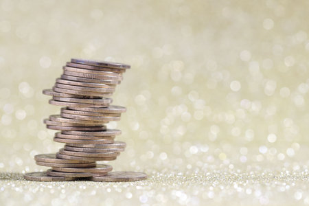 Many stacked coins on golden glitter background, closeup. Space for textの写真素材